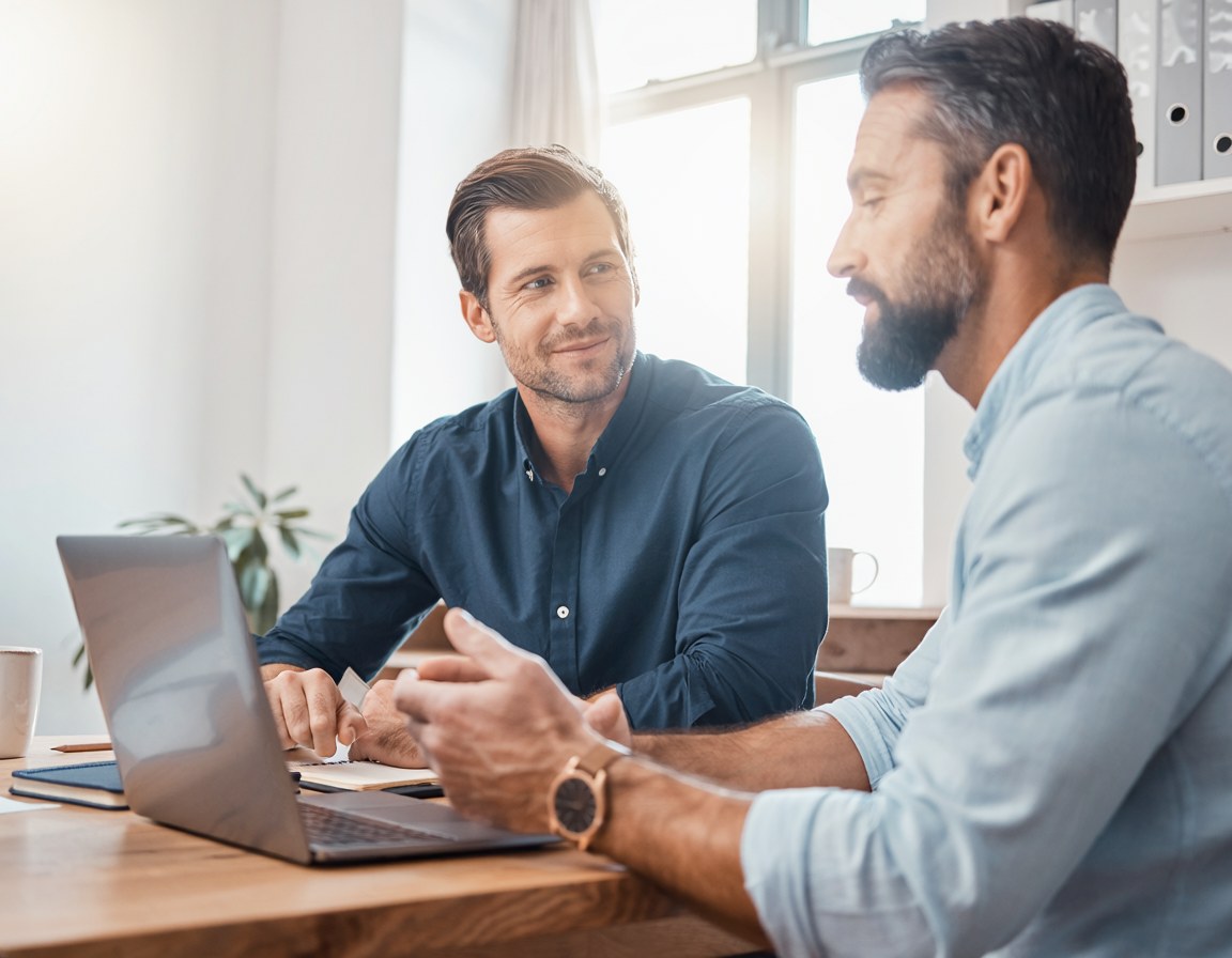 Two people at a table talking through something on a laptop